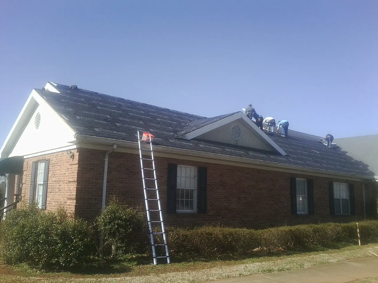 Crew tearing shingles off a brick ranch roof with a ladder set — Emergency Roof Repair work by our crew in Homer Glen