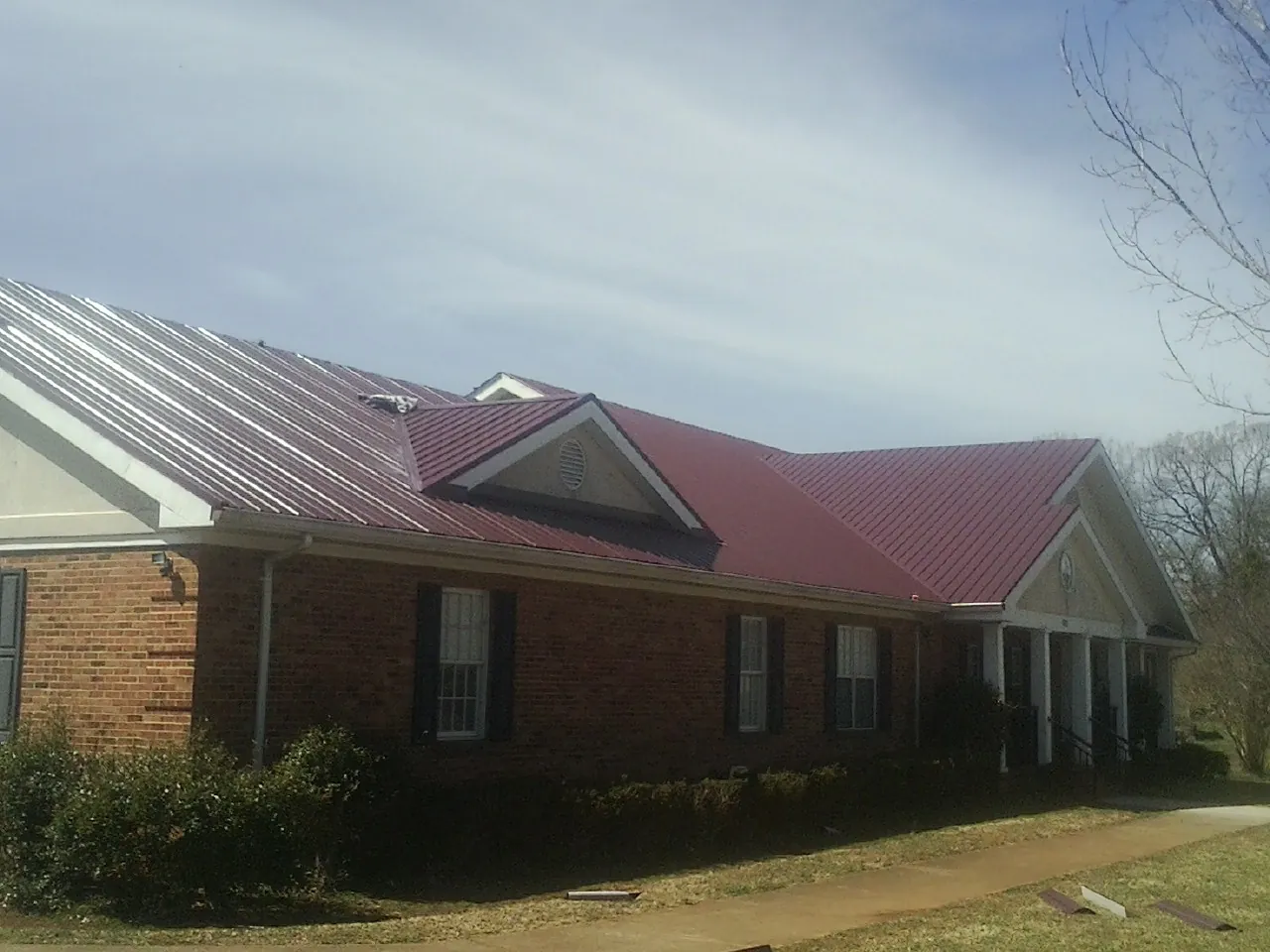 Red metal roof with gabled entries on a long brick building, from a Hail Damage Roof Repair job in Homer Glen