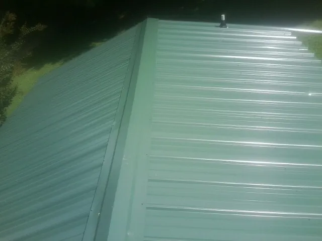 New green metal panels meeting at the ridge of a roof — Flat Roof Repair work by our crew in Homer Glen