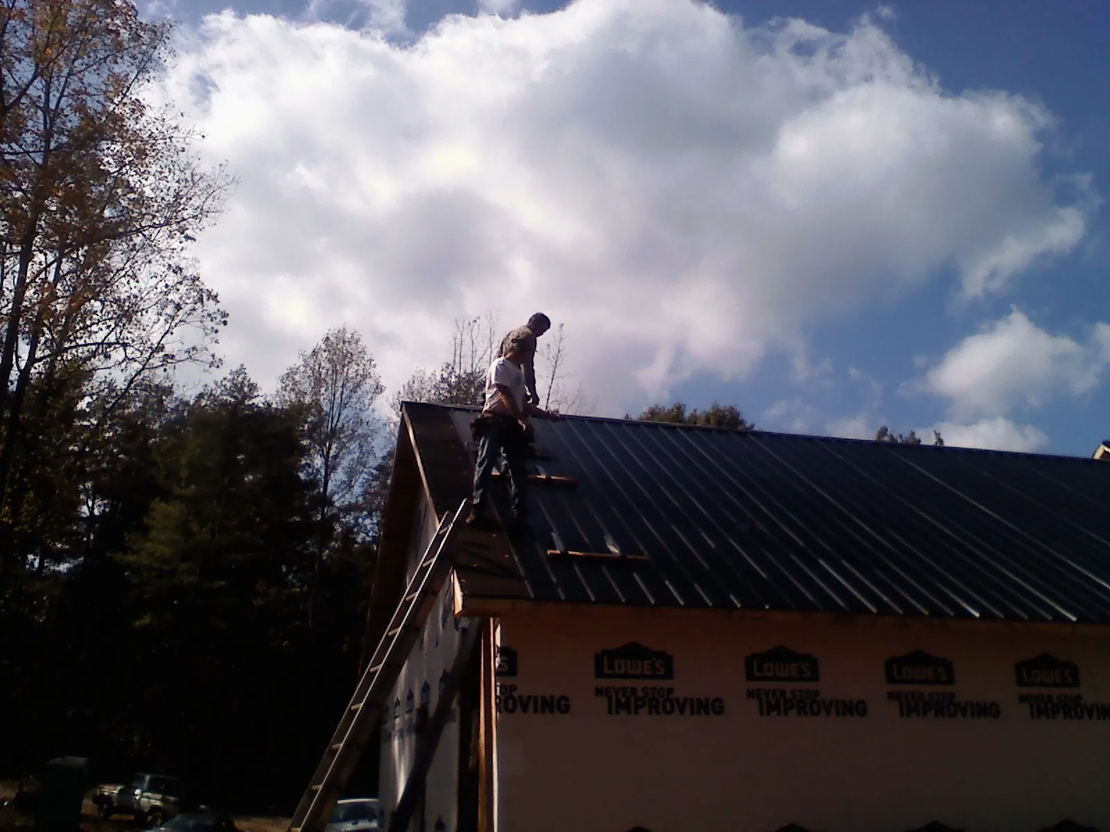 Roofer fastening dark metal panels high against a cloudy sky, from a Roof Inspection job in Homer Glen