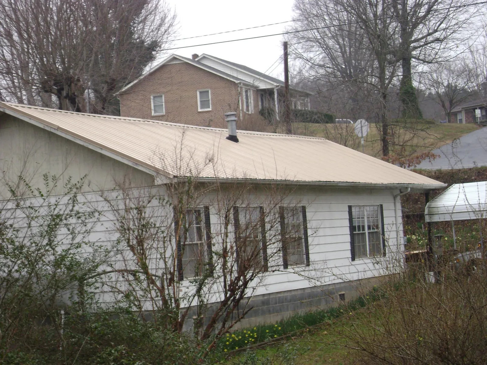 Tan metal roof on a white sided house set into a hillside — Commercial Roofing by Roofing Brothers in Homer Glen